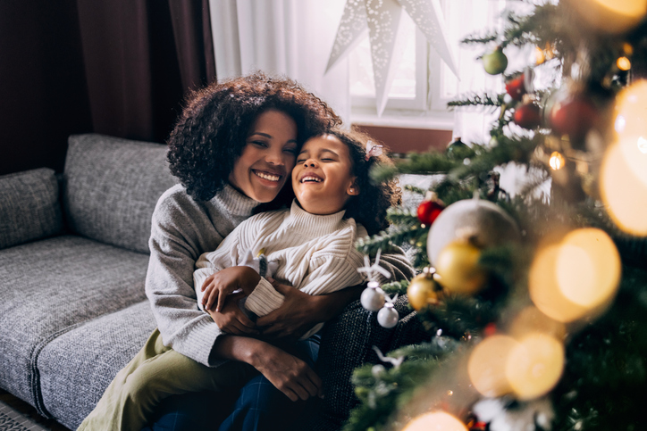 Mother and daughter sitting on couch smiling next to Christmas tree