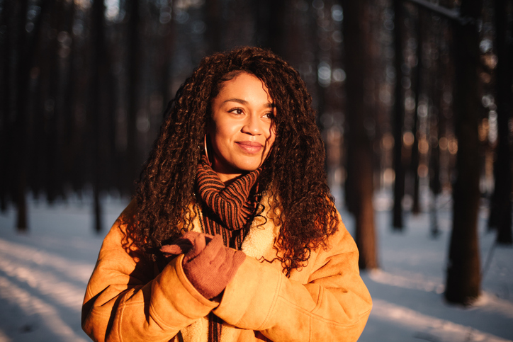 Happy young woman looking at sun standing in park during winter