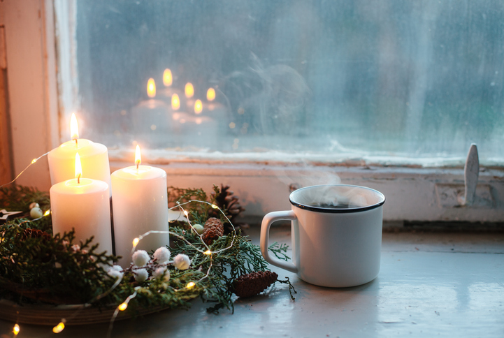 White candles, coffee mug and pine branch wreath on window sill